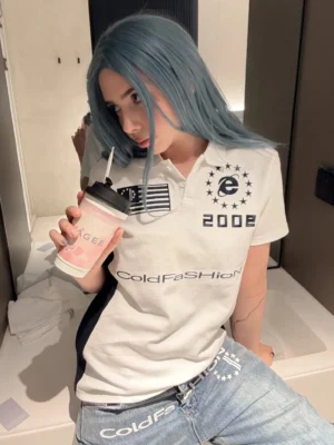 White and navy 2002 varsity crest polo shirt styled on a female model with retro chest graphics in a casual indoor streetwear setting