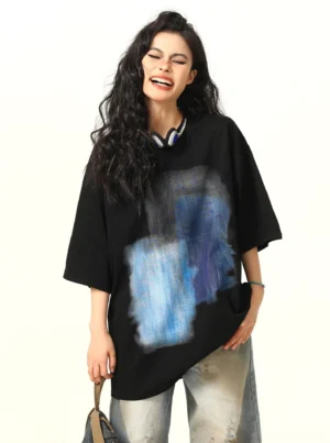 Front view of a black abstract blue watercolor oversized T-shirt styled with wide-leg jeans, headphones, and a small handbag for a Seoul streetwear outfit