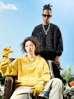 Two models wearing abstract outline embroidered oversized crewneck sweatshirts in black and mustard yellow streetwear styling outdoors