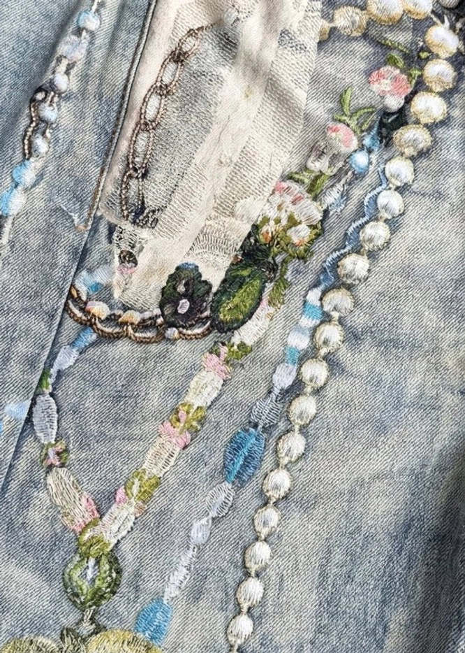 Close-up of acid wash denim jort front with floral embroidery pearl chains metal chain accents and distressed patches