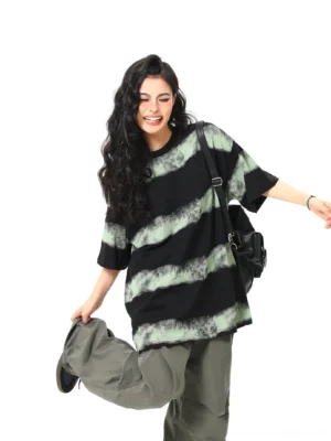 Three-quarter side view of an oversized black and mint-green acid wash striped streetwear T-shirt styled with loose grey cargo pants and a crossbody bag