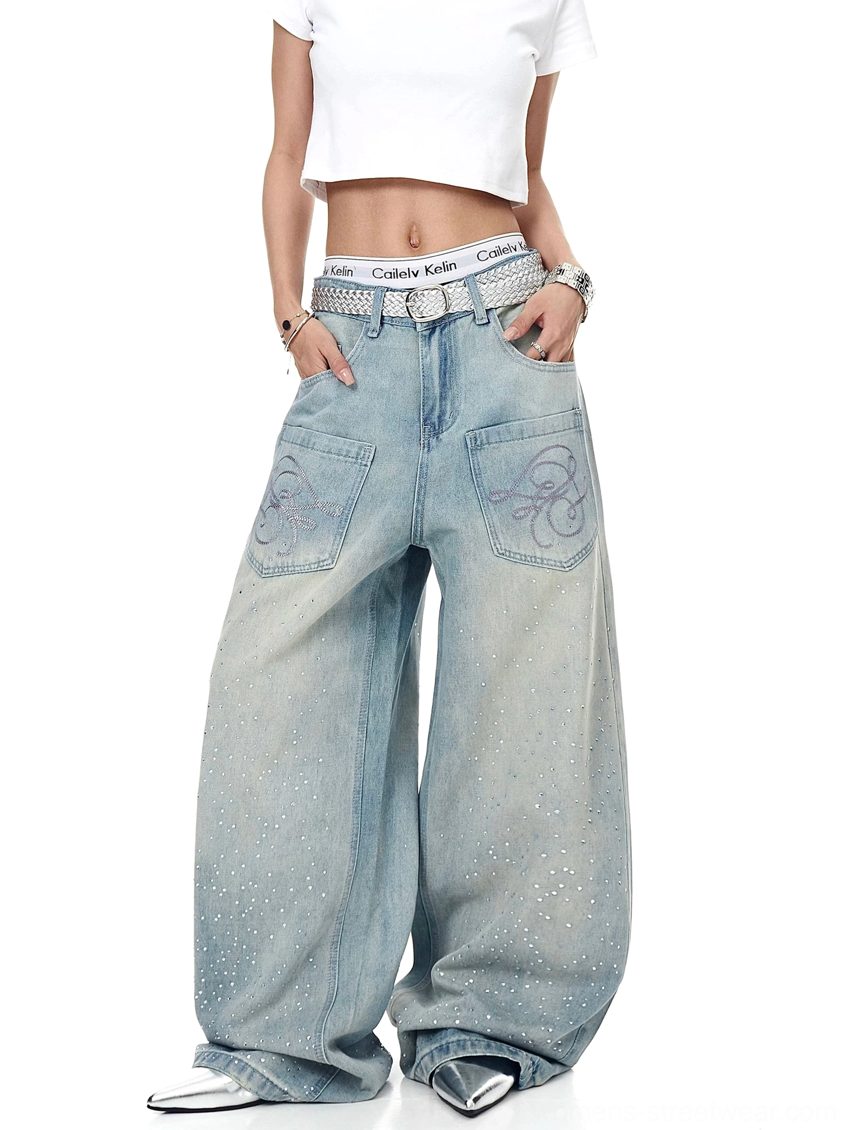 Relaxed front view of acid-washed blue Y2K jeans with oversized wide legs, embroidered patch pockets, rhinestone sparkle, silver belt, and cropped white top