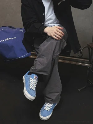 Sky blue embroidered skate sneakers worn with a black jacket, white tee, loose gray cargo pants, and a blue tote bag in a modern streetwear outfit