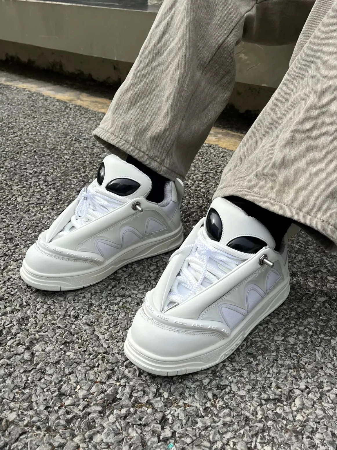 Alien head platform sneakers on foot with gray trousers and black socks, low-angle urban streetwear view