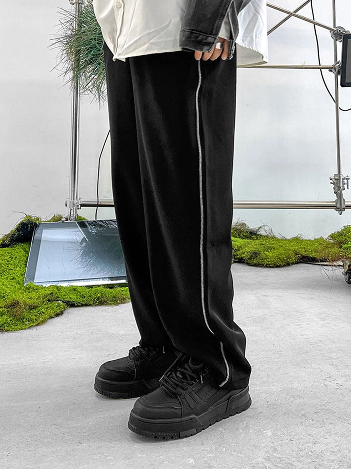All-black chunky platform sneakers styled with layered streetwear clothing and wide-leg pants in an industrial fashion setting