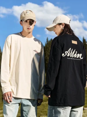 Couple wearing ivory white and black alpine script oversized cotton long sleeve streetwear tees in an open grassland