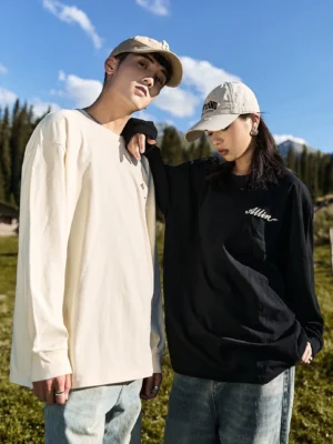 Side view of matching black and ivory alpine script graphic long sleeve cotton tees styled for outdoor streetwear