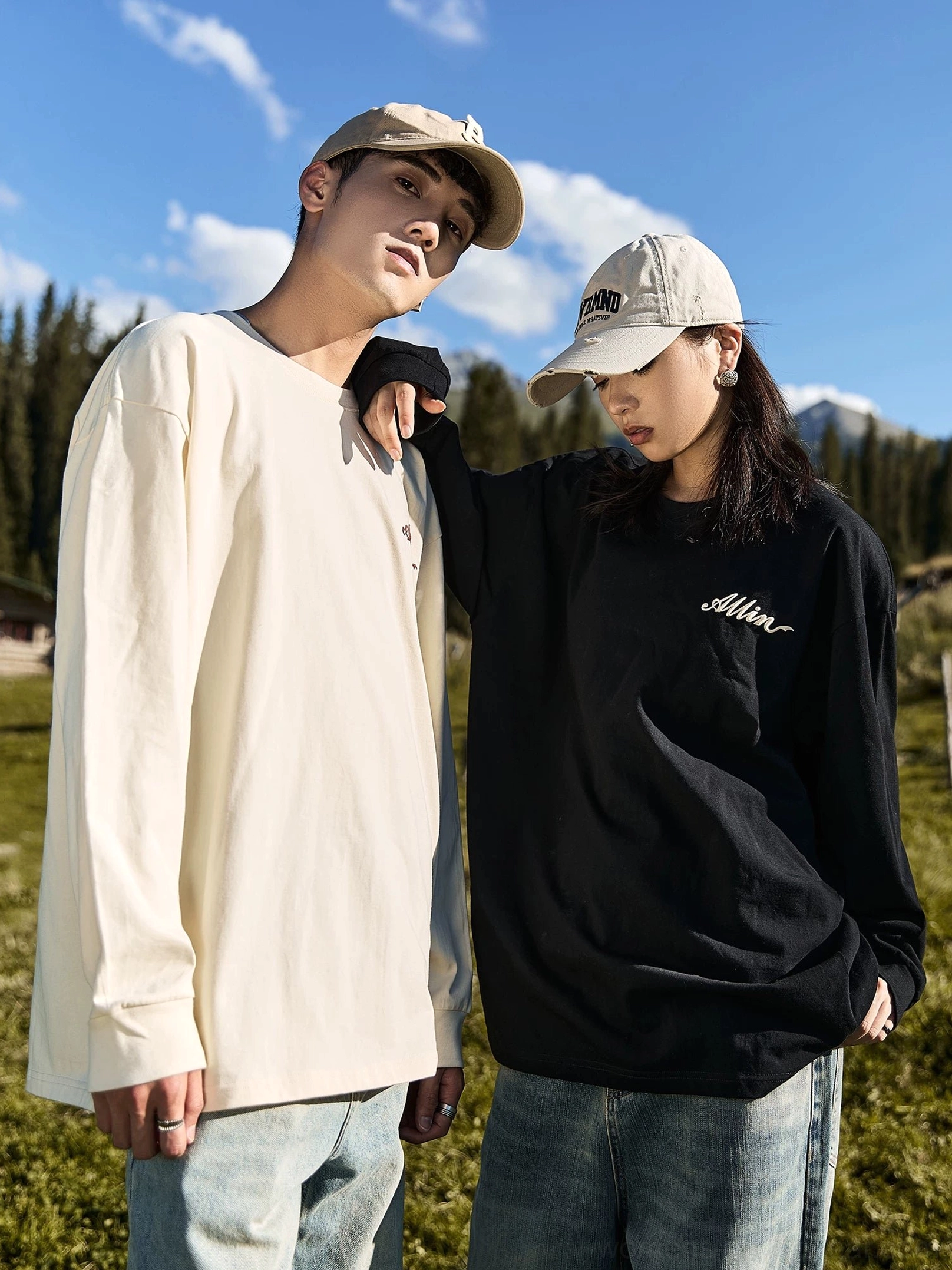 Side view of matching black and ivory alpine script graphic long sleeve cotton tees styled for outdoor streetwear