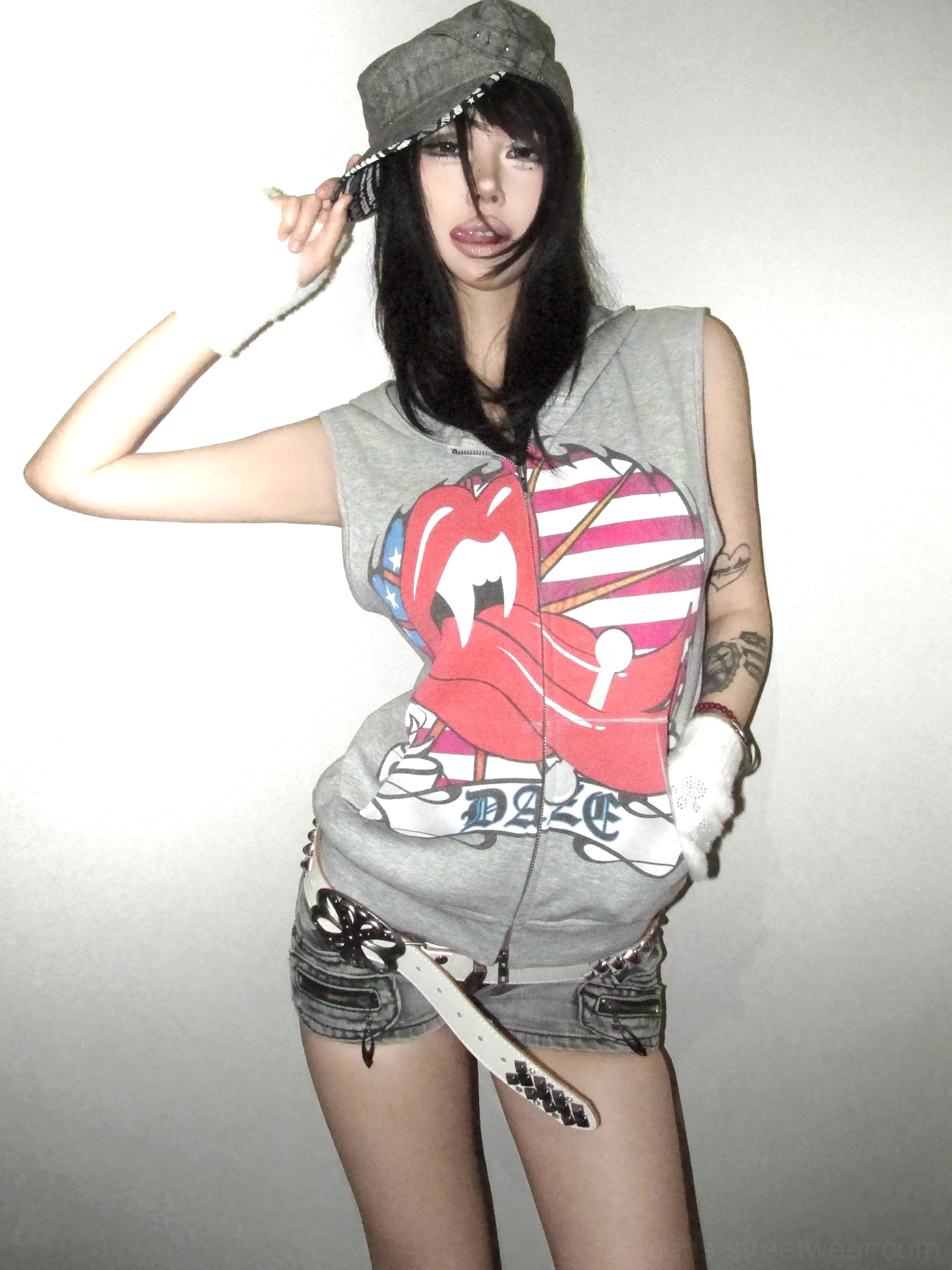 Female model wearing a heather gray Americana flag lips graphic sleeveless zip-up hoodie vest in a minimalist studio