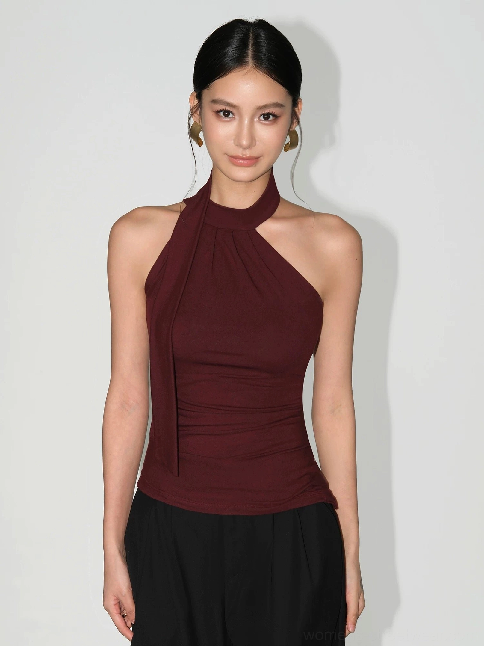 Angolan red asymmetric halter knit top with high neckline, sleeveless fitted silhouette, and gathered torso styled with black wide-leg pants