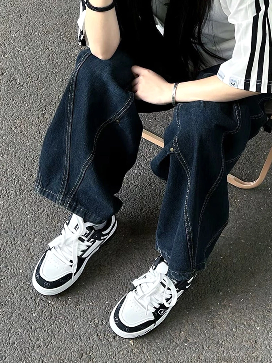 Black and white cat print low-top sneakers worn by seated model with relaxed baggy jeans streetwear styling
