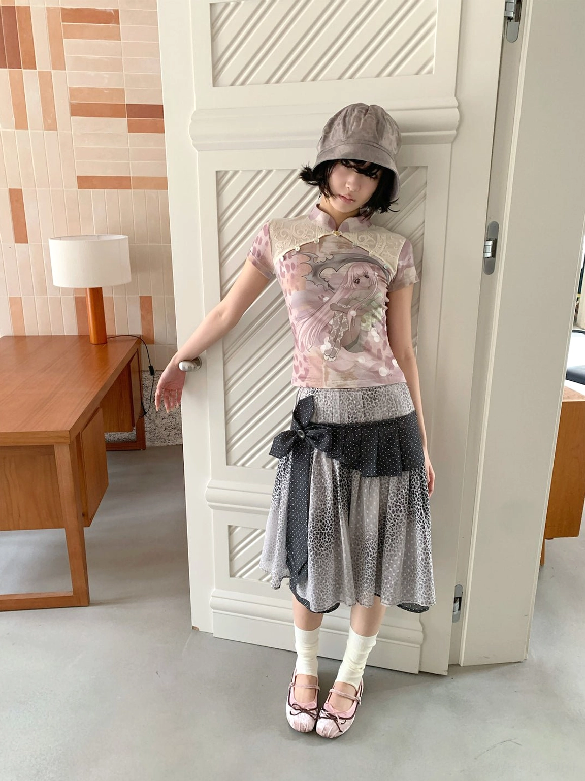 Female model in a grey bucket hat wearing a fitted anime print cheongsam collar tee with a patchwork tulle skirt