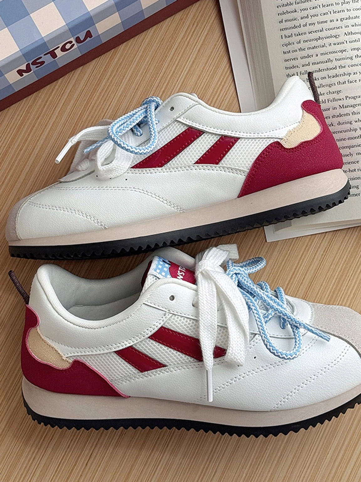 Apple detail red mesh retro runner sneakers displayed on a wooden table with books and a blue checkered shoe box