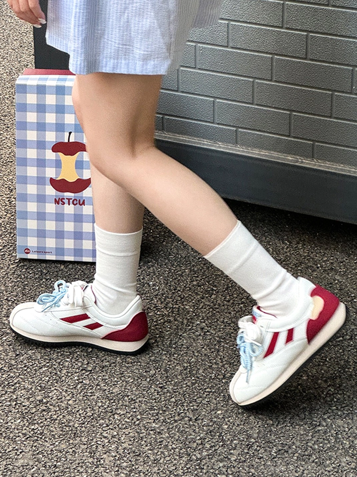 Women wearing apple detail red mesh retro runner sneakers with white crew socks on an outdoor asphalt street