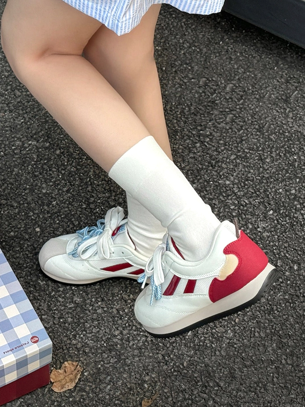 Top view of apple detail red mesh retro runner sneakers worn with white socks beside a blue checkered shoe box