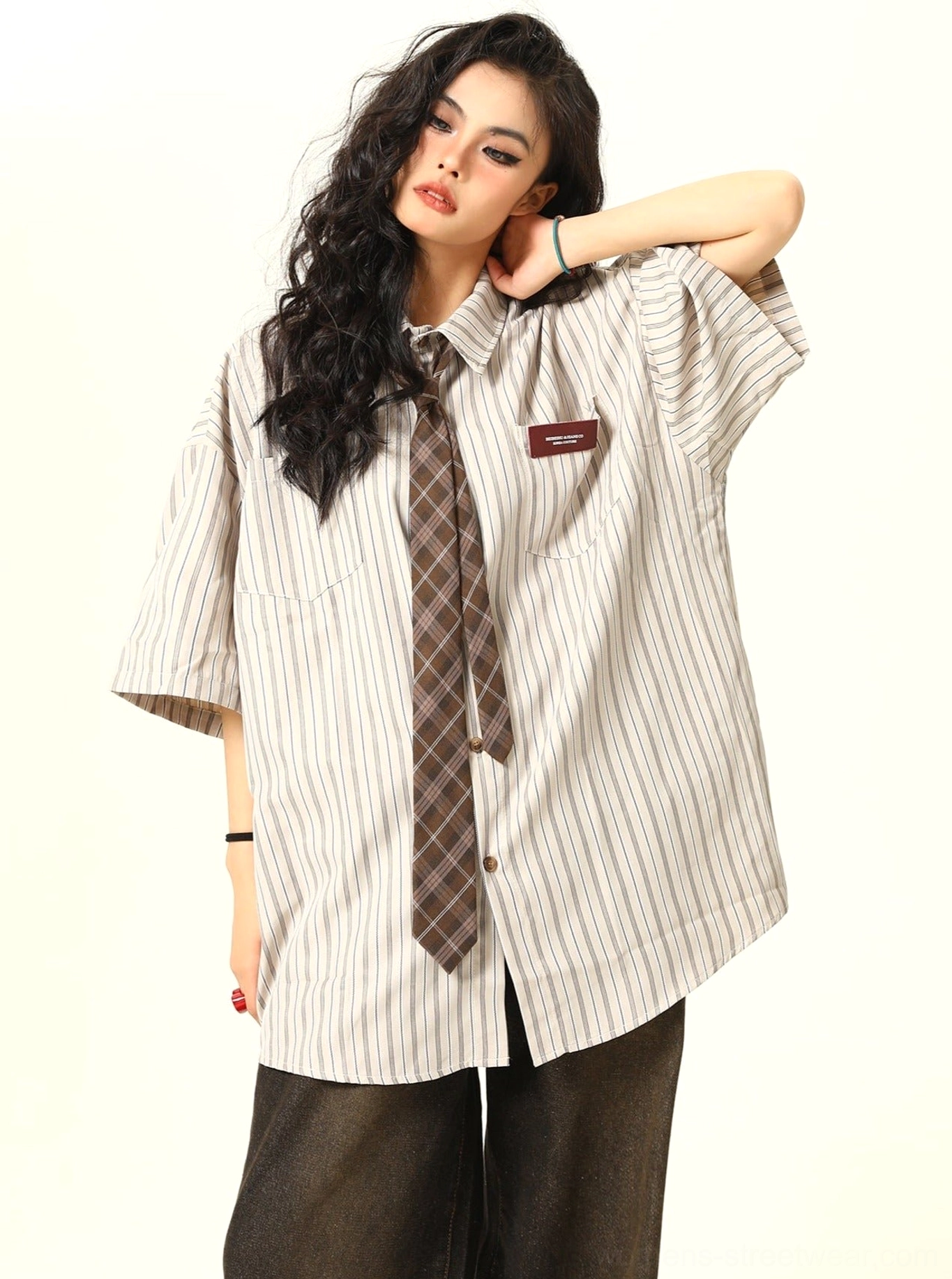 Three quarter view of an apricot cream striped oversized button up shirt with drop shoulders, chest patch, and brown plaid tie