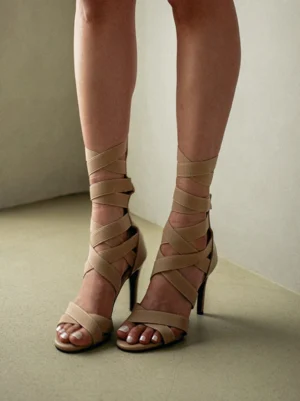 Apricot gladiator stiletto sandals worn on female feet showing open toe, wrapped ankle straps, and slender high heels