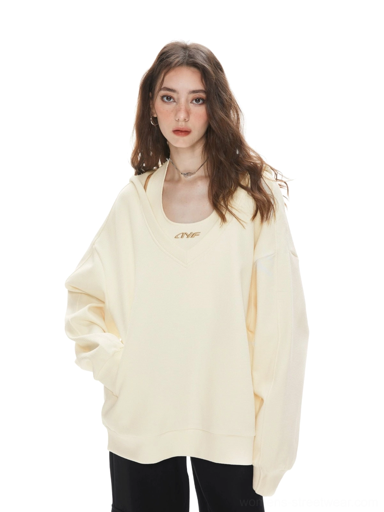 Apricot oversized V-neck hoodie sweatshirt with subtle chest emblem, drop shoulder fit, and black straight-leg pants styling
