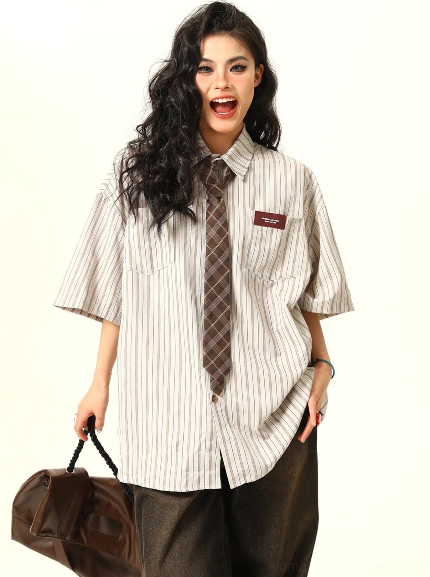 Female model wearing an apricot cream striped oversized short sleeve shirt with brown plaid tie and dark brown wide leg trousers