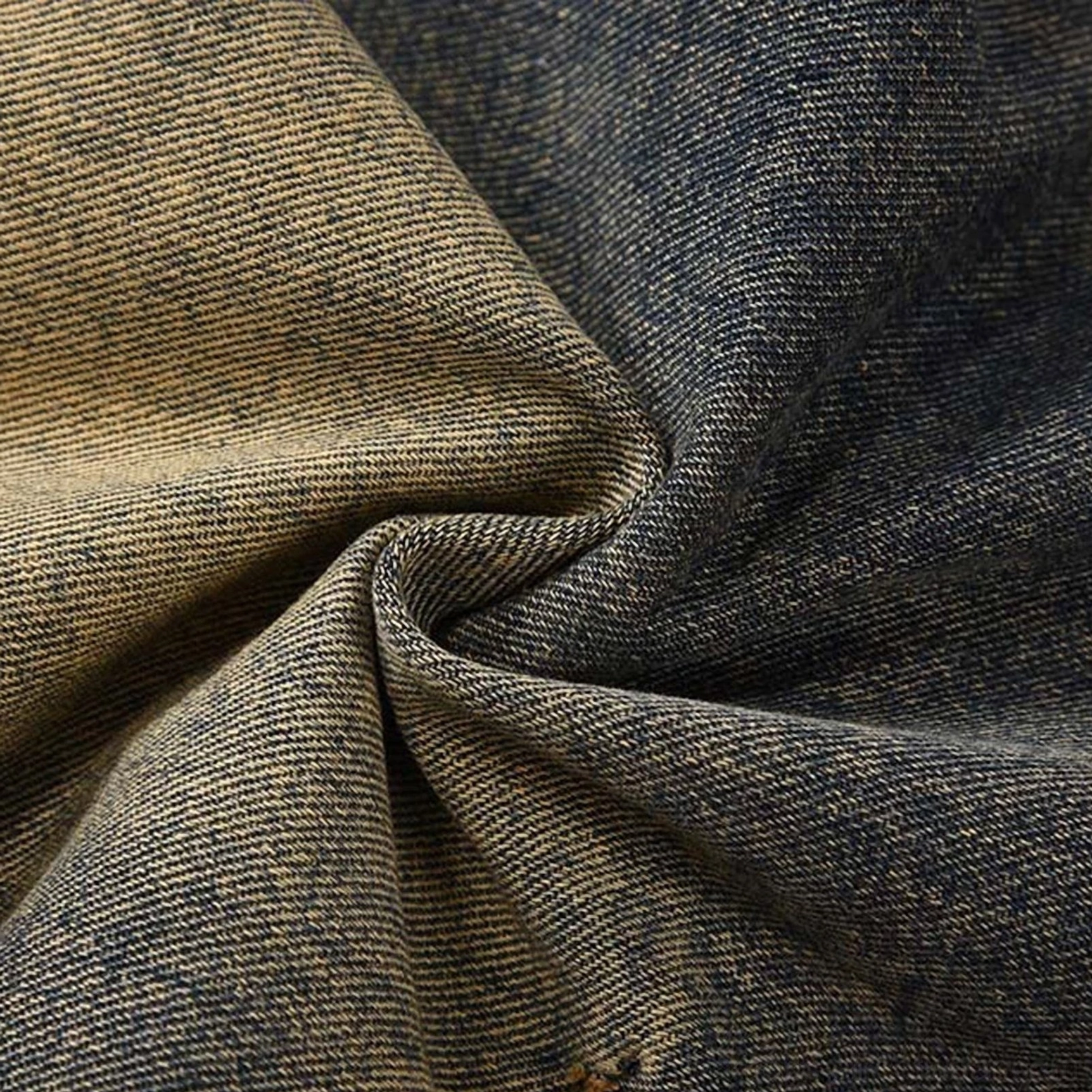 Macro close-up of architectural acid wash denim fabric showing classic twill weave, mixed indigo and yellow faded tones, and softly crushed texture