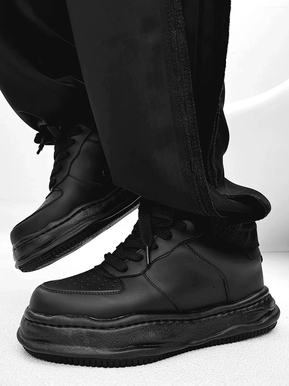 Arctic Crest all-black chunky platform sneakers with distorted sole worn with baggy black trousers