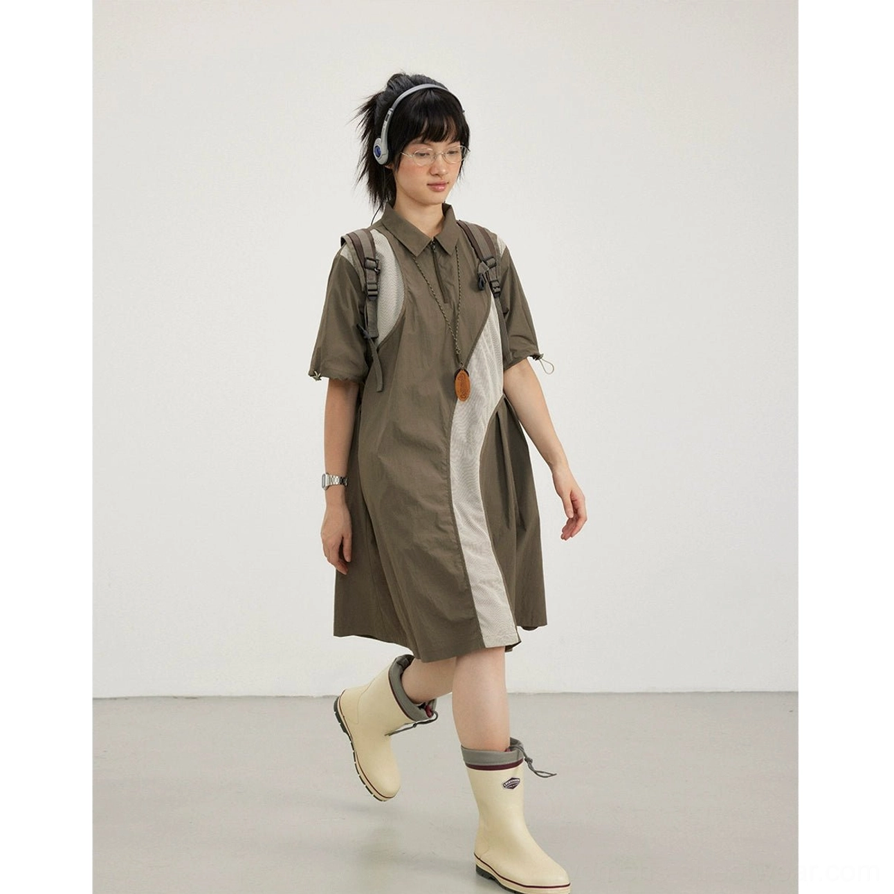 Army brown oversized knee-length shirt dress styled with knee-high rain boots and backpack straps