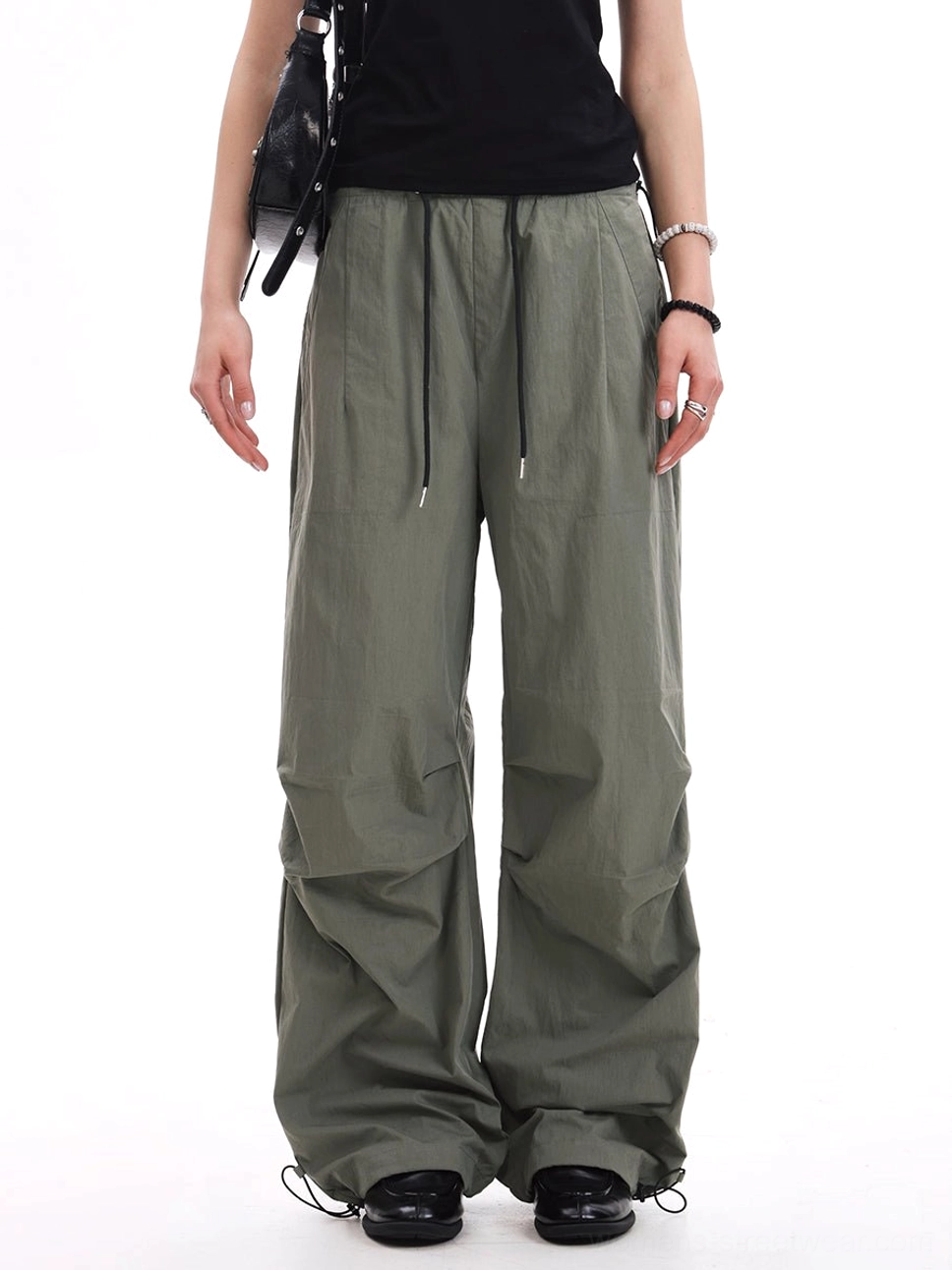 Army green oversized parachute pants showing adjustable drawstring details and gathered ankle cuffs in a contemporary streetwear outfit
