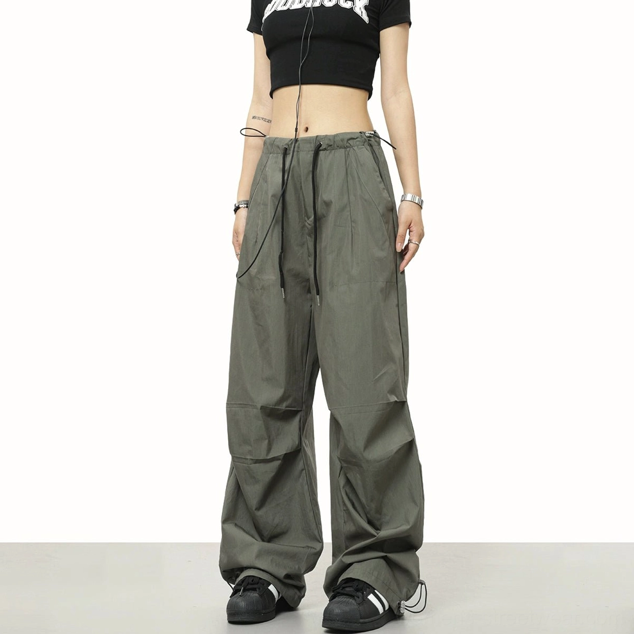 Army green parachute streetwear pants shown from the side with front pleats, wide-leg silhouette, and adjustable drawstring waist