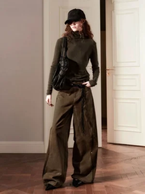 Full-body streetwear outfit featuring brown artisan stitch wide-leg pants, fitted dark green turtleneck, black baseball cap, and leather crossbody bag