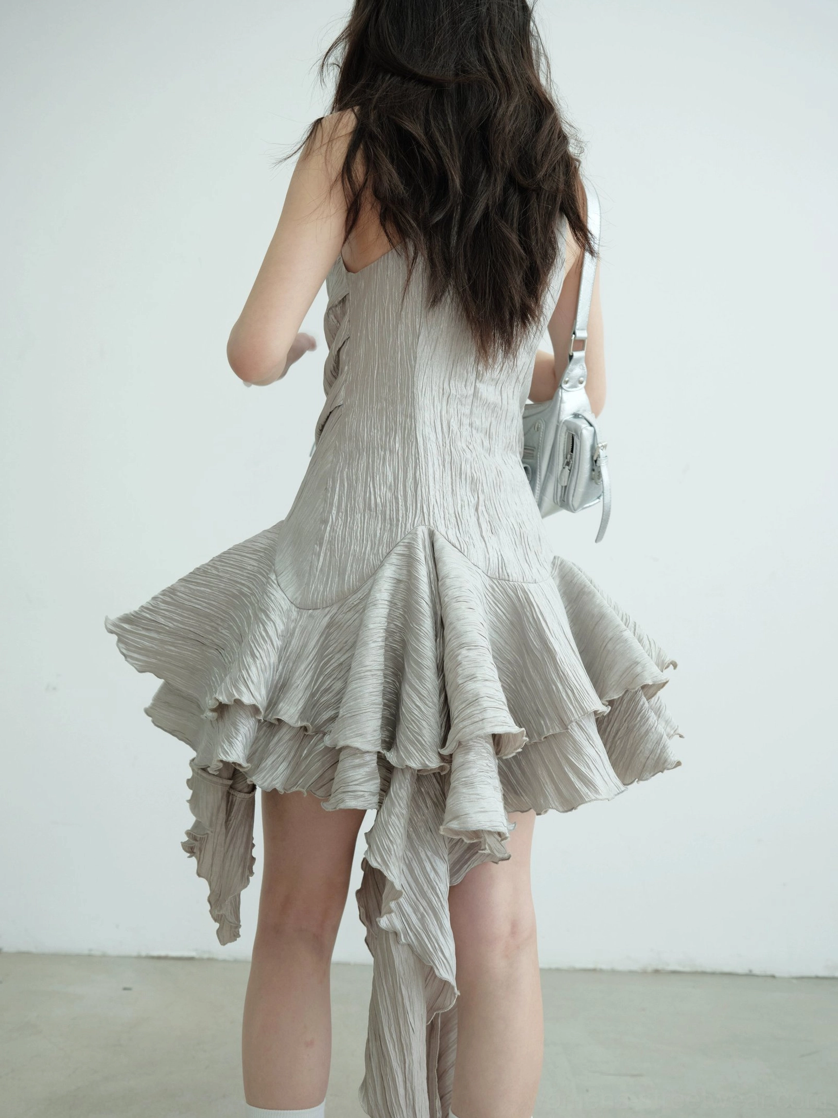 Rear side view of an ash asymmetric metallic party mini dress showing crinkled fabric and voluminous layered ruffle hem