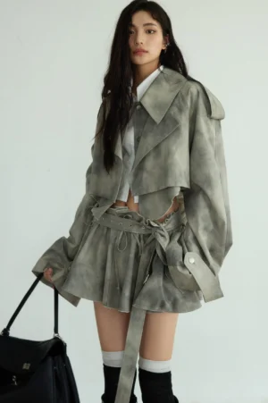 Ash gray cropped trench coat and matching mini skirt outfit styled with a waist cutout, thigh-high socks, black heeled boots, and a black leather tote bag