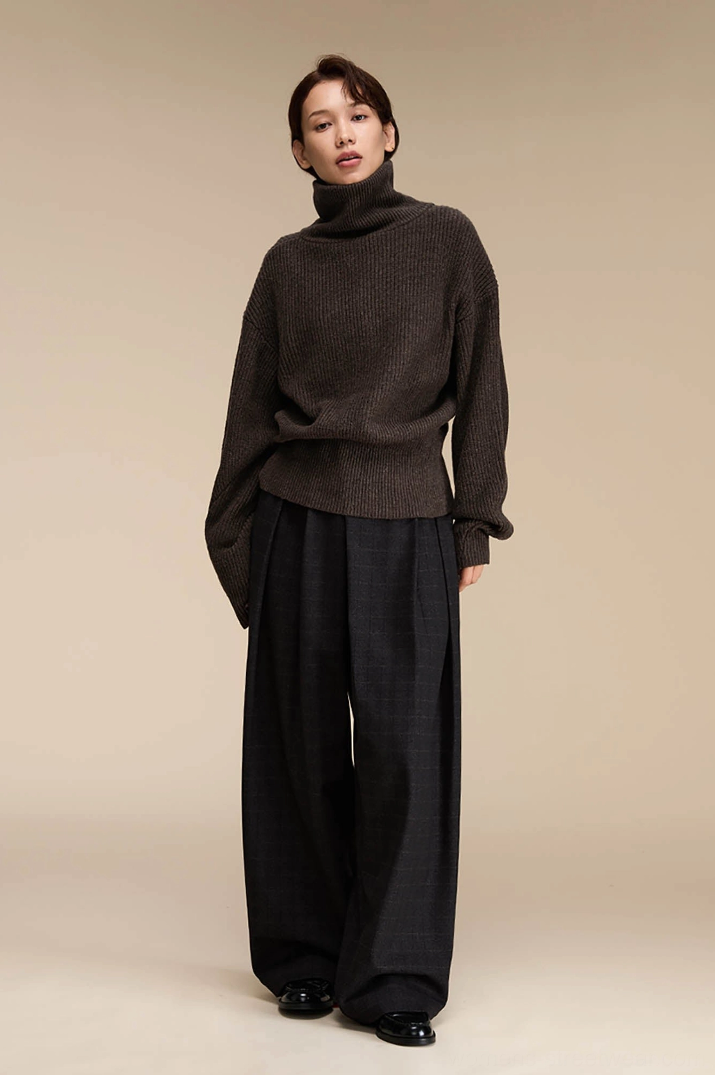 Asian female model wearing dark grey plaid wide-leg suit pants with a brown turtleneck and black leather shoes