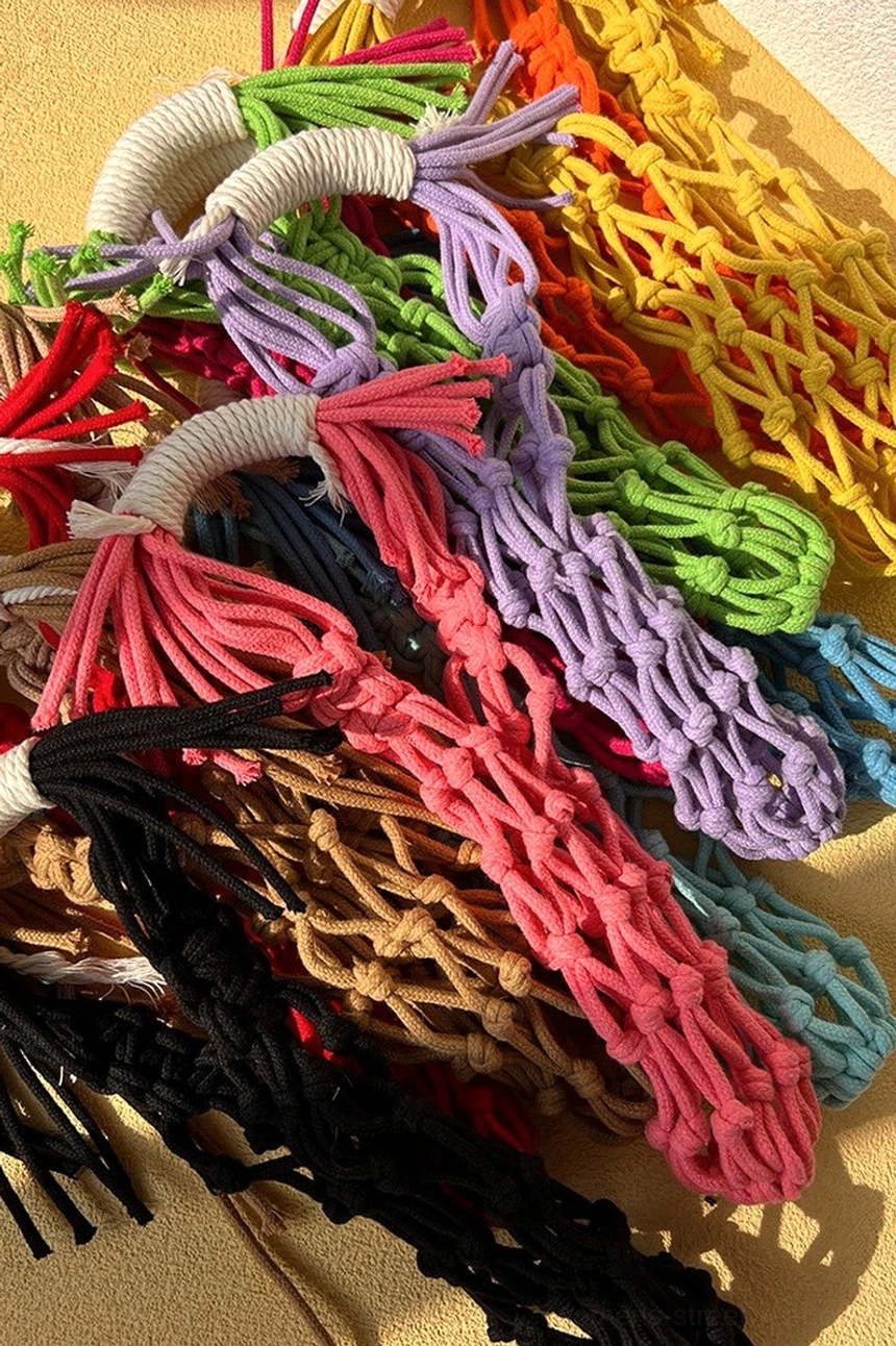 Assorted colorful cotton macrame water bottle carriers arranged together in pink, purple, yellow, green, black, and brown streetwear accessory colors