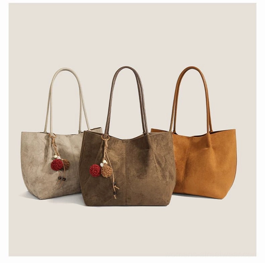 Assorted faux suede pom charm tote bags in off-white, dark taupe, and caramel brown colorways for Acubi streetwear outfits