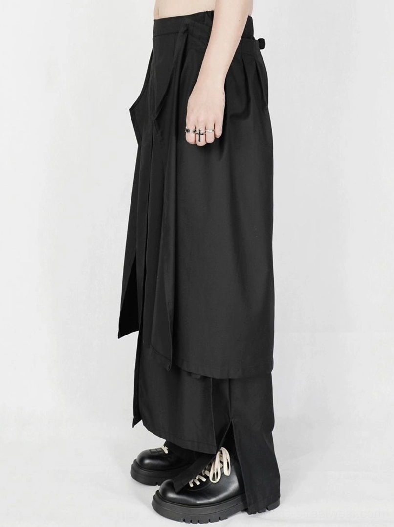 Close-up side view of asymmetric apron-style draped black wide-leg streetwear trousers with platform shoes
