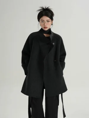 Front full-body view of a women's dark charcoal wool streetwear coat with asymmetric stand collar, relaxed raglan sleeves, side pockets, waist belt, and mid-length cocoon silhouette