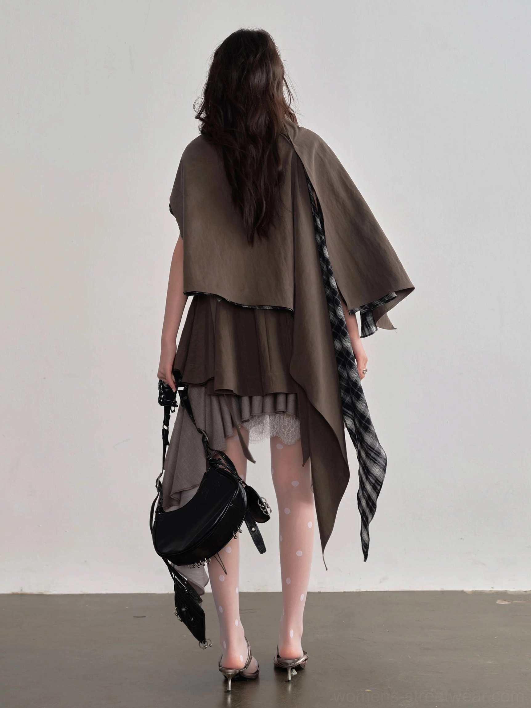 Back view of asymmetric coffee brown cape layer blouse featuring exposed plaid drape, flowing panels, and an irregular hem styled with sheer tights and heels