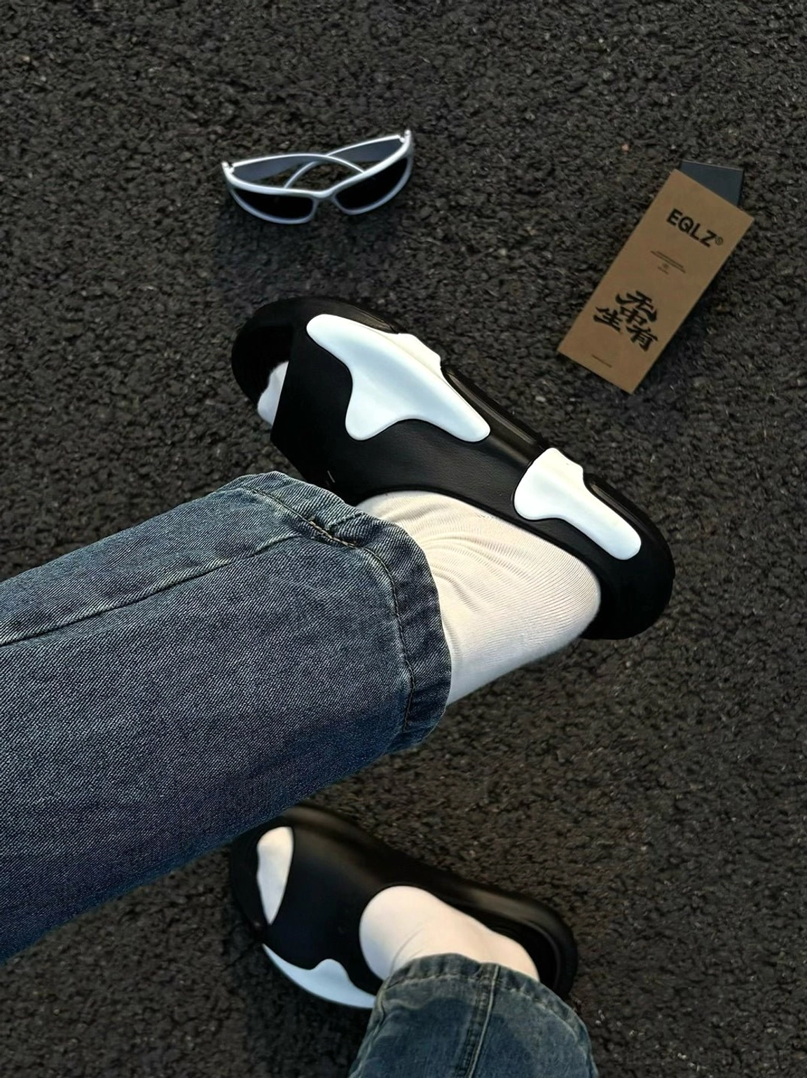 Streetwear outfit detail featuring black and white asymmetric colorblock cloud cushion slide sandals with denim jeans