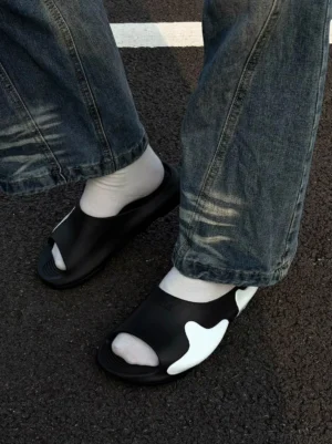 Asymmetric black and white colorblock cloud cushion slide sandals worn with white socks and blue jeans on city pavement