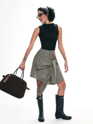 Asymmetric gingham check button-down wrap skirt styled with black tank top and knee-high boots in a studio side view