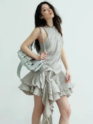 Front three-quarter view of an asymmetric metallic ruffle hem party mini dress with halter neckline, crinkled texture, three-dimensional floral detail, and silver shoulder bag