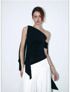 Front view of a navy velvet asymmetric one-shoulder draped streetwear top with long side sash styled with white wide-leg pants
