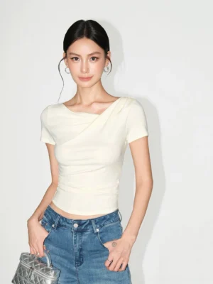 Cream asymmetric off-shoulder ruched slim fit top styled with blue denim jeans in a minimalist studio