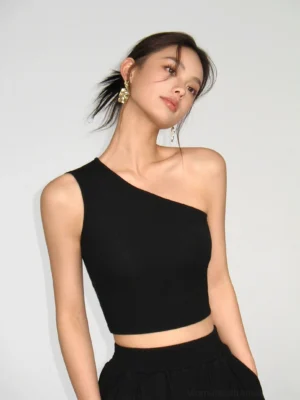 Black asymmetric one-shoulder stretch knit crop top styled with black wide-leg pants in a minimalist studio