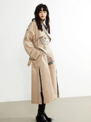 Three quarter side view of khaki patchwork trench coat with belted waist, shoulder epaulets, side pocket, lower zipper slit, and black platform boots