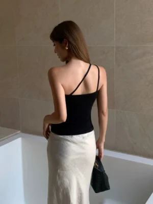 Black asymmetric one shoulder ribbed knit top back view styled with a satin skirt and black handbag