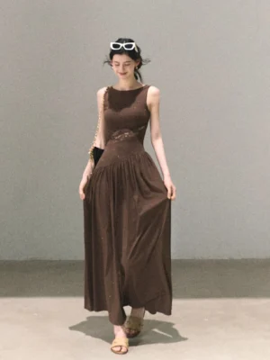 Chocolate brown asymmetrical lace waist maxi dress with sleeveless boat neckline and flowing floor-length skirt in a studio setting