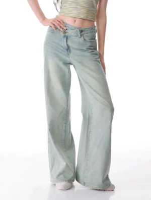 Front view of women's asymmetrical light wash wide leg jeans with slanted crossover waistband and vintage blue denim finish