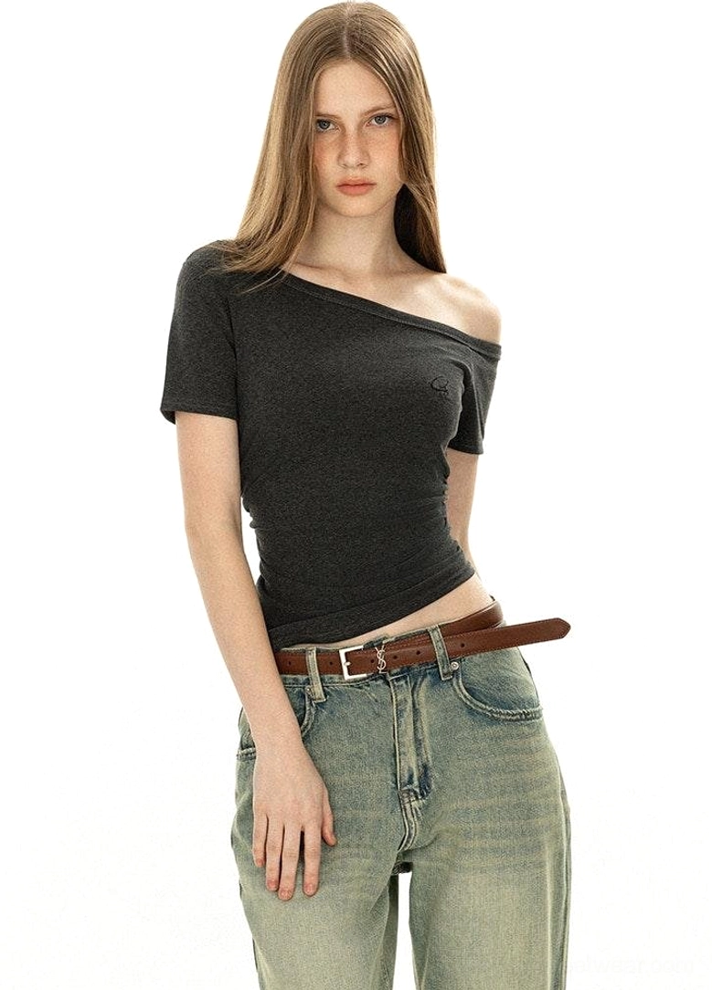 Side profile asymmetrical off-shoulder dark grey basic tee with short sleeves and embroidered chest logo paired with vintage denim