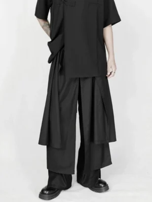 Front full-body view of avant-garde asymmetric draped wide-leg black streetwear trousers in a white studio